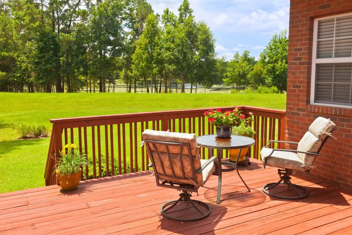 Stained wood deck with railings, a table and chairs beside a green lawn
