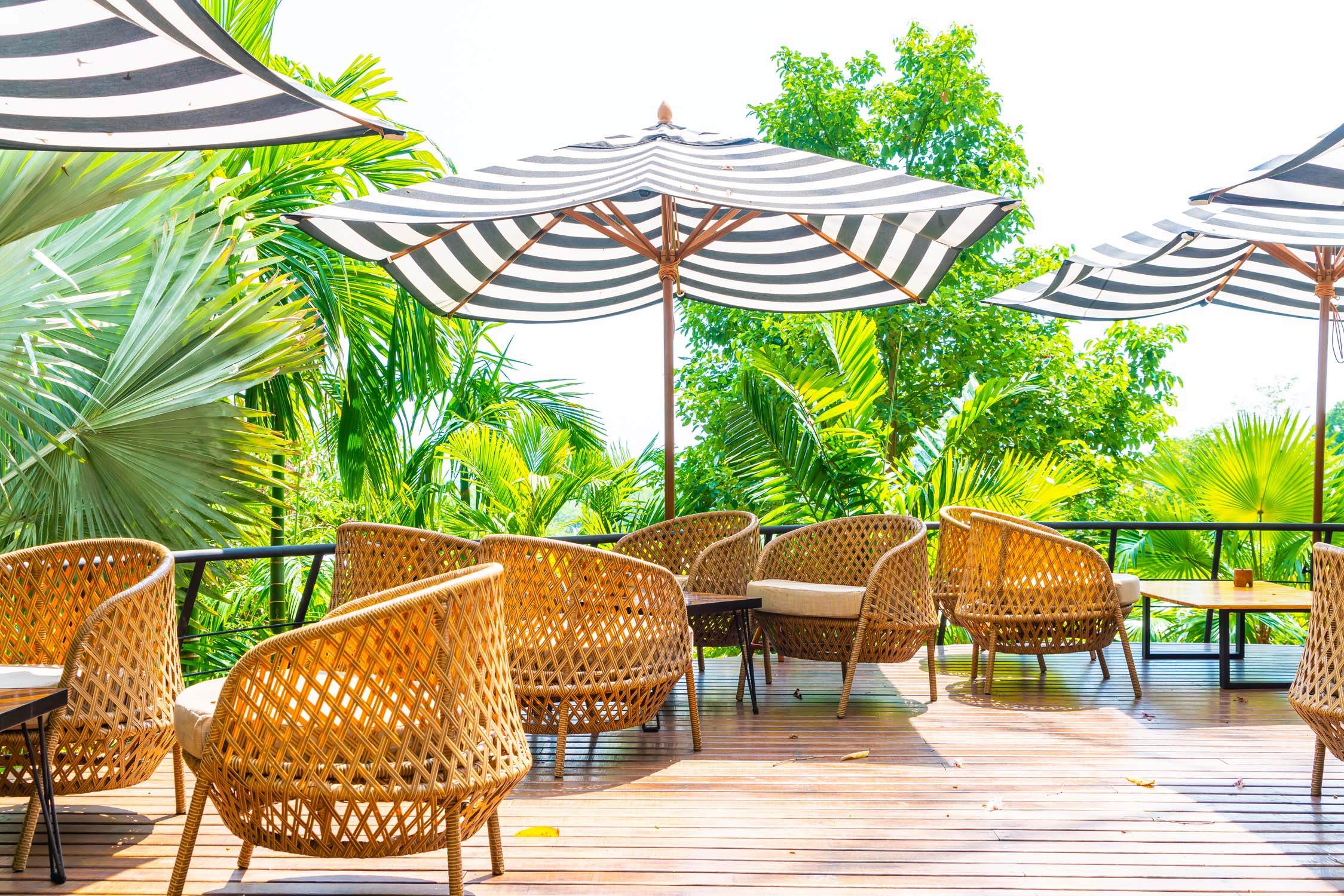 Decked terrace with striped parasols and rattan seating beside planting