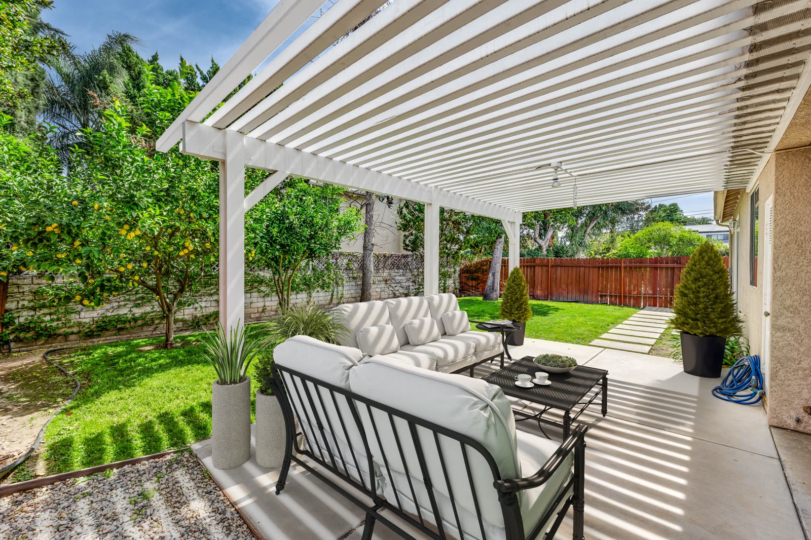 White pergola over a patio seating area beside a planted garden