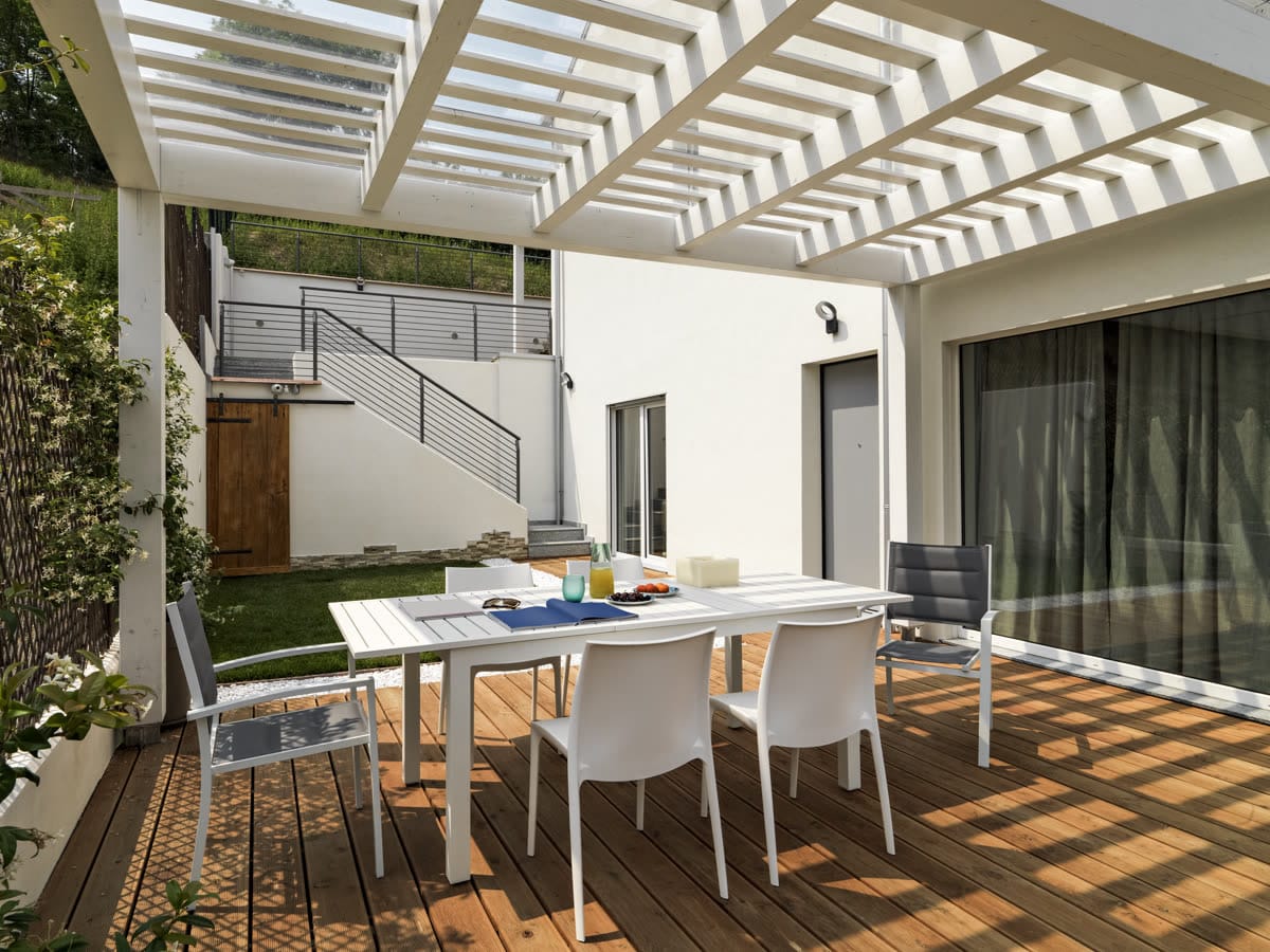 White dining set under a slatted pergola on a paved terrace