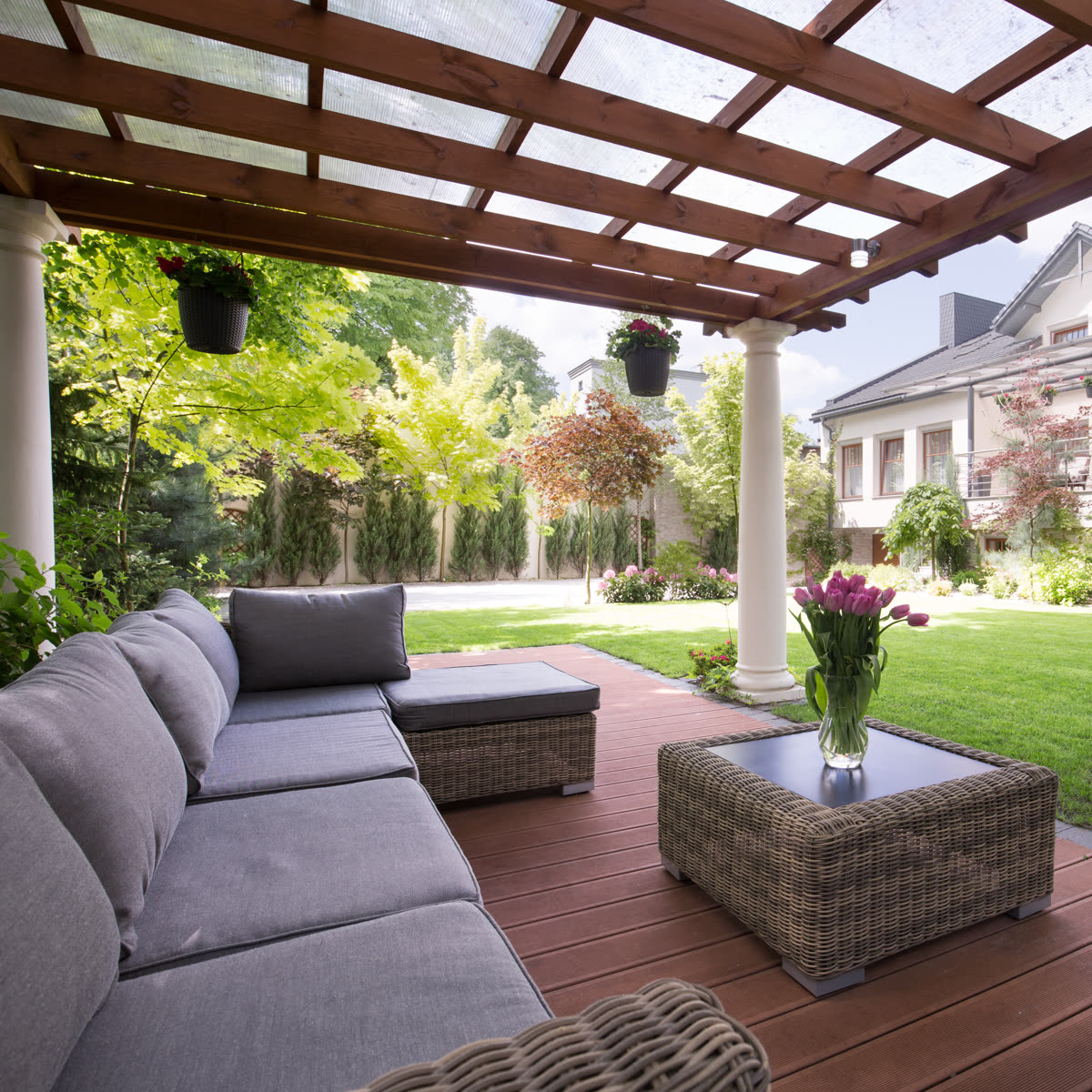 Grey sectional under a pergola beside a clipped lawn