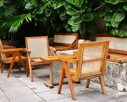 Teak outdoor chairs and table on a stone patio surrounded by lush tropical planting