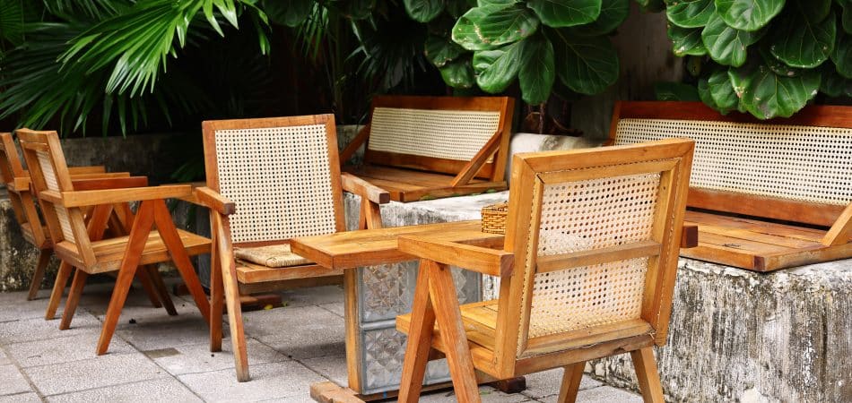 Teak outdoor chairs and table on a stone patio surrounded by lush tropical planting