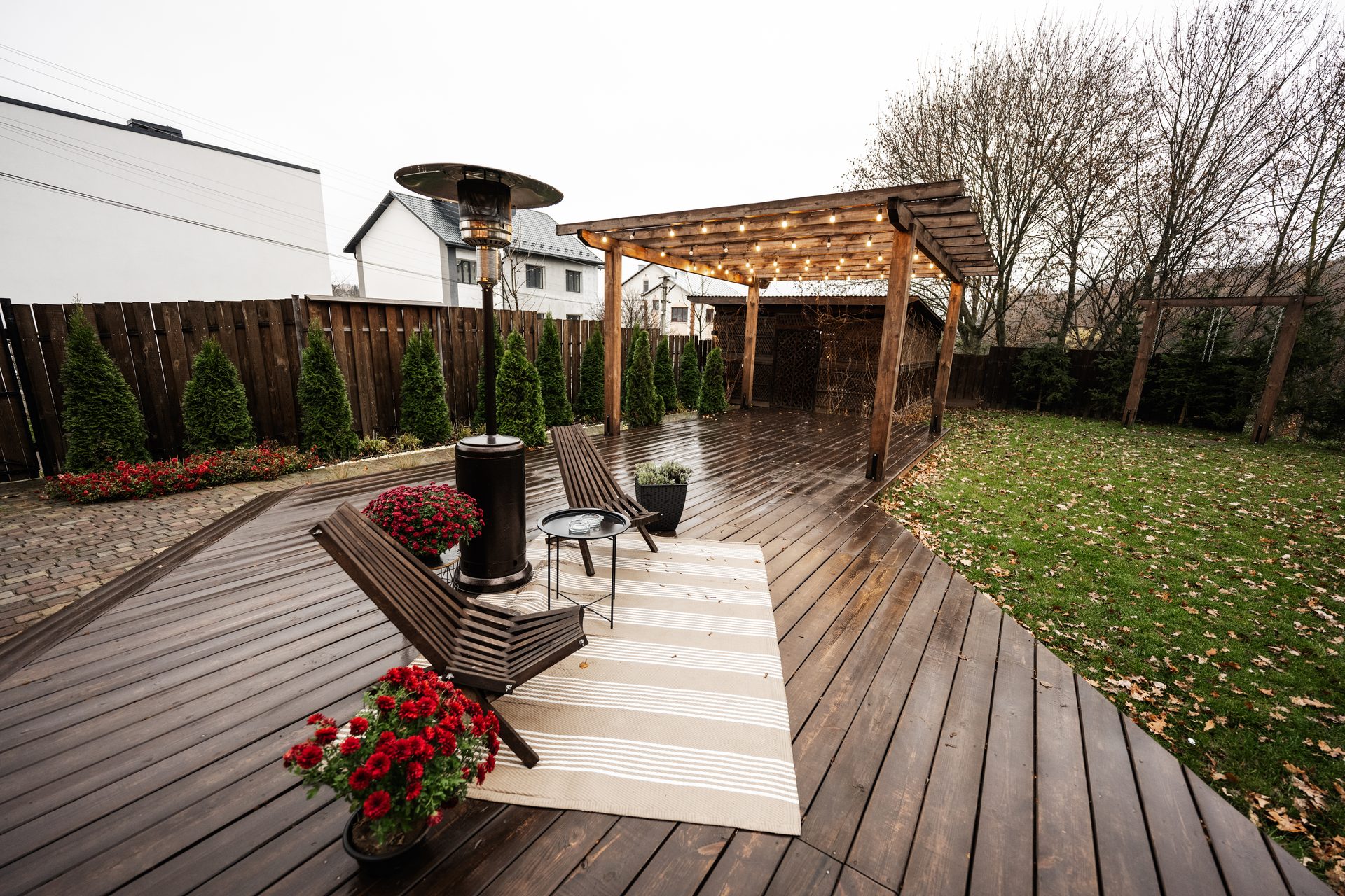 Covered deck with a patio heater, string lights and lounge chairs beside a lawn