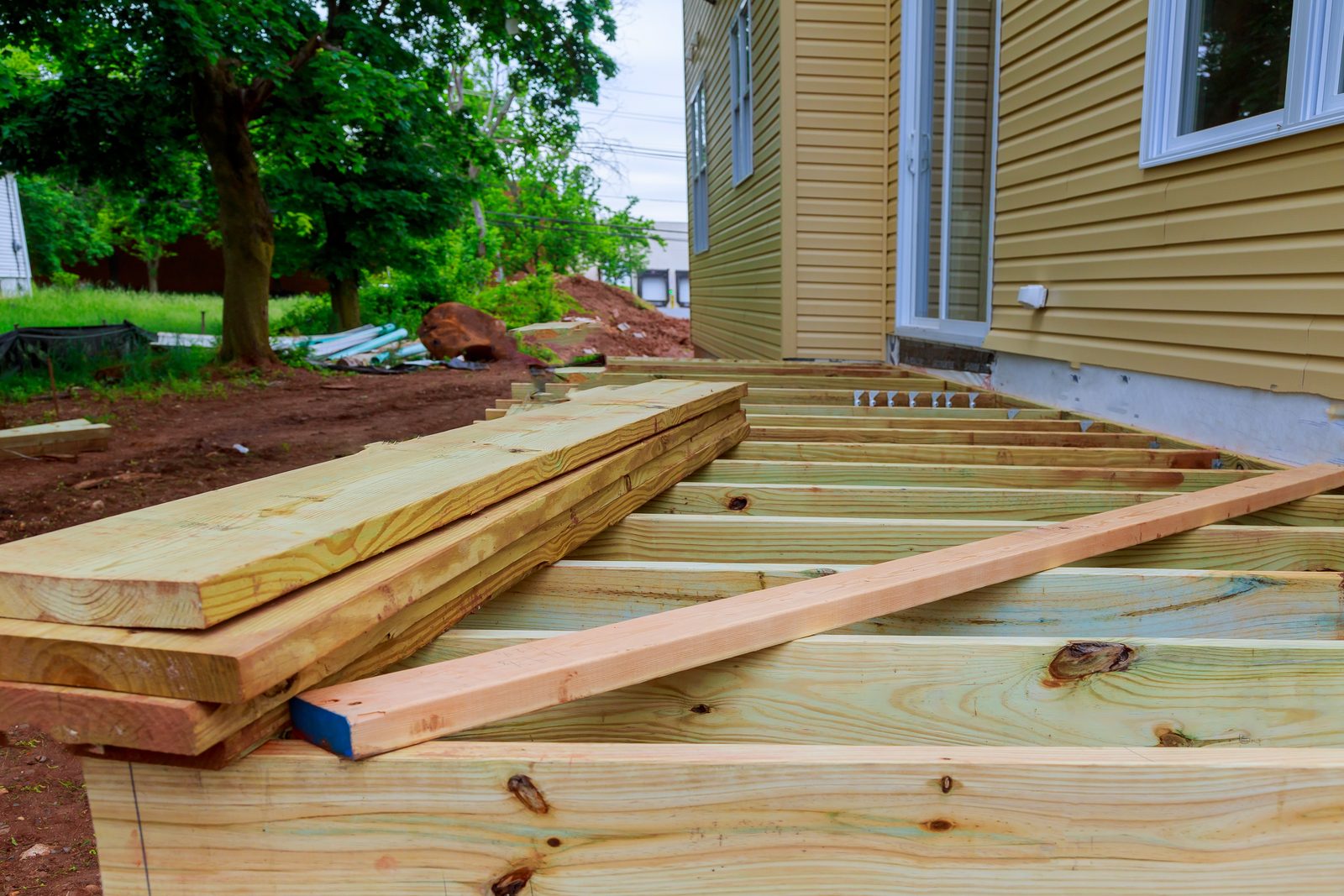 New deck framing and stacked lumber against the back of a house