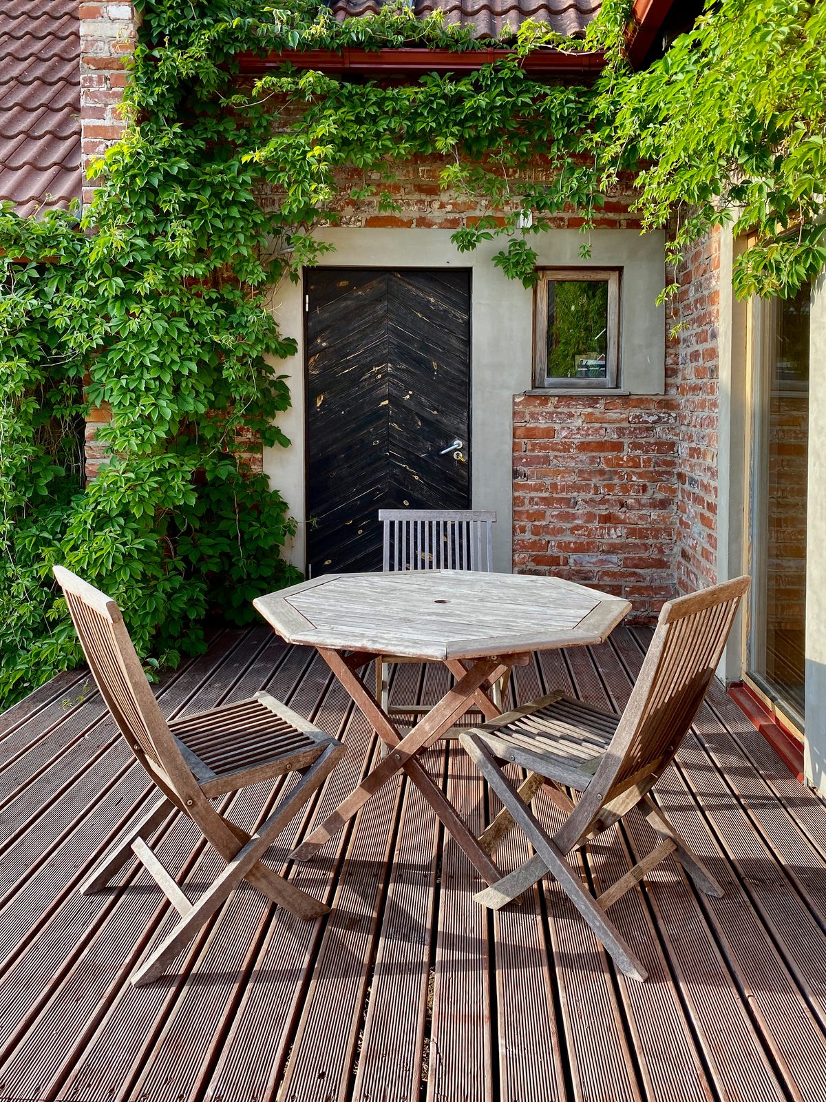 Wooden table and chairs on a paved patio beside planting