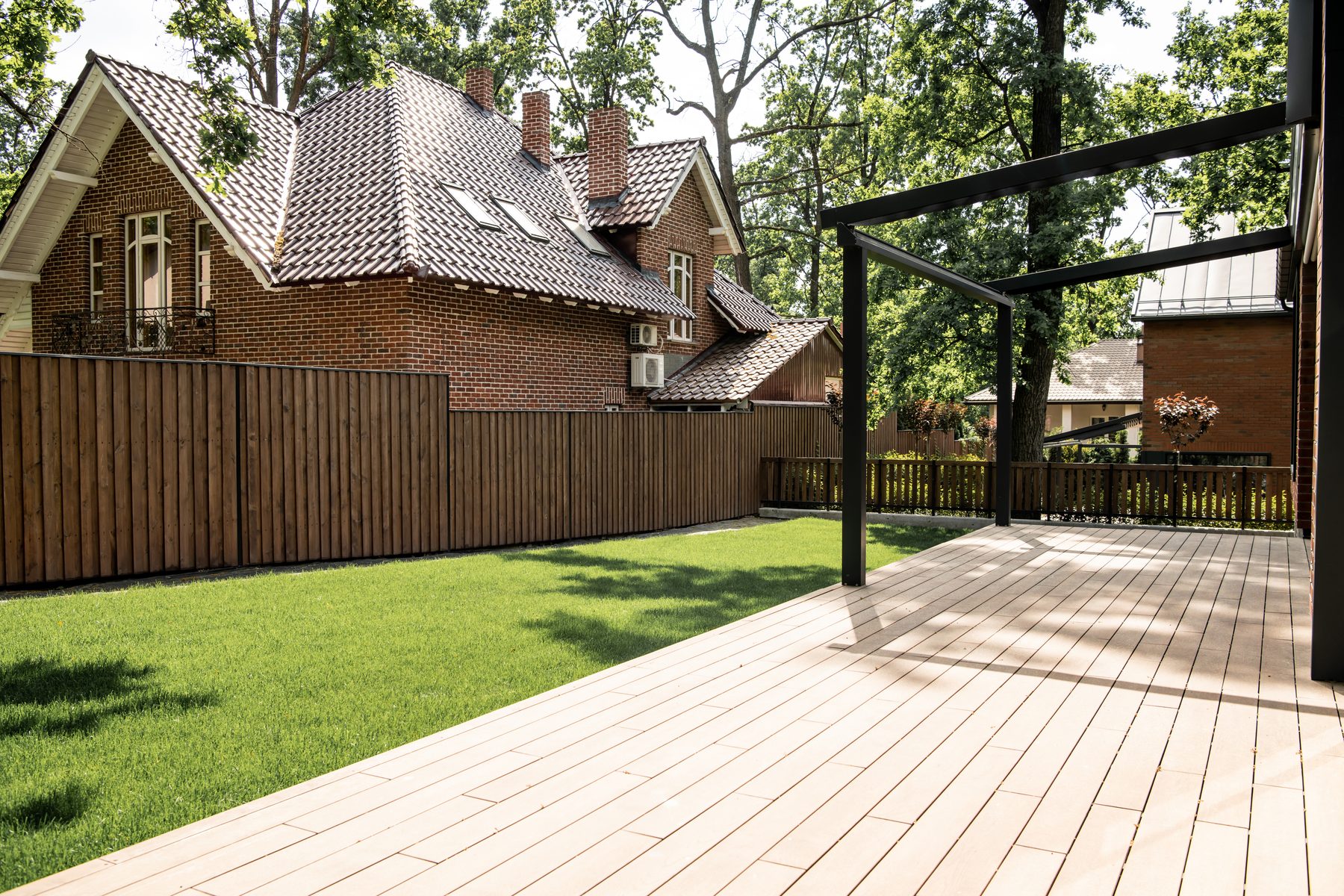 New wood deck behind a brick house with a fenced lawn