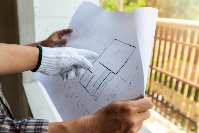 Gloved hands holding construction plans outdoors beside a railing